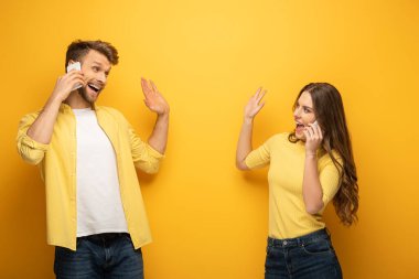 Sarı arka planda akıllı telefonlardan bahsederken neşeli çift el sallıyor.