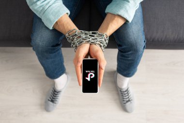 KYIV, UKRAINE - 21 Şubat 2020: Kanepenin üzerinde TikTok uygulaması ile akıllı telefonu tutan metal zincirli adam manzarası 