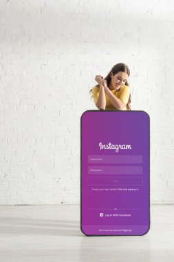 KYIV, UKRAINE - 21 Şubat 2020: Evde instagram uygulaması olan büyük akıllı telefon modeline bakan mutlu kız 