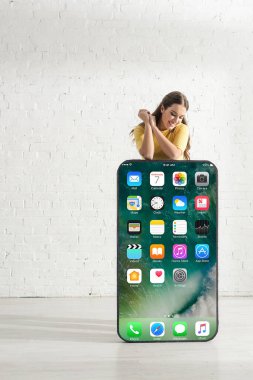 KYIV, UKRAINE - 21 Şubat 2020: iPhone ekranlı akıllı telefonun büyük bir modelinin yanında gülümseyen çekici kız 