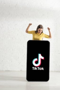 KYIV, UKRAINE - 21 Şubat 2020: Evet işareti yapan neşeli kız TikTok uygulamalı akıllı telefonun yanında