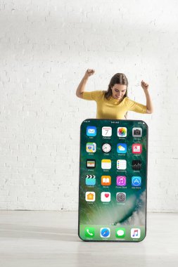KYIV, UKRAINE - 21 Şubat 2020: Pozitif kız iPhone ekranlı büyük akıllı telefon modeline bakarken evet hareketi gösteriyor 