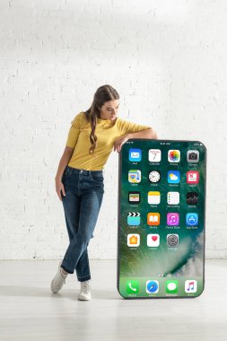 KYIV, UKRAINE - 21 Şubat 2020: Evde iPhone ekranlı akıllı telefon modeline bakan çekici kız 