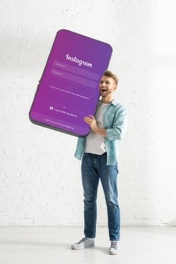 KYIV, UKRAINE - 21 Şubat 2020: Instagram uygulamalı akıllı telefonun büyük modelini elinde tutan mutlu adam 