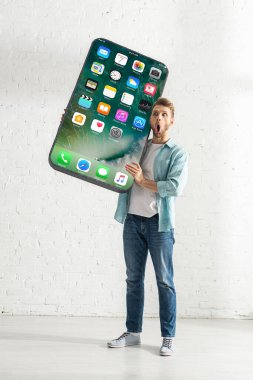 KYIV, UKRAINE - 21 Şubat 2020: Evde iPhone ekranı ile büyük bir akıllı telefon modeli tutan şok adam 