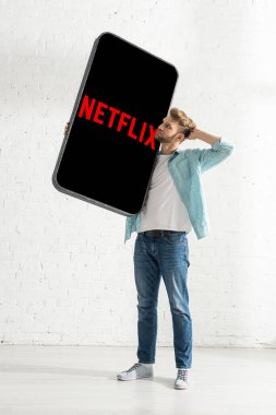 KYIV, UKRAINE - 21 Şubat 2020: Netflix uygulamalı akıllı telefonun büyük modelini elinde tutan düşünceli adam 