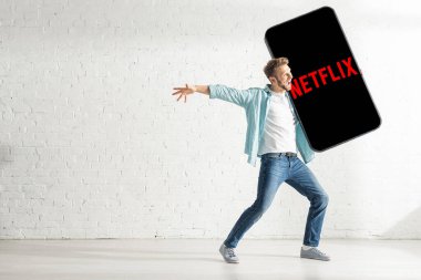 KYIV, UKRAINE - 21 Şubat 2020: Oturma odasında Netflix uygulamalı akıllı telefonun büyük modelini tutan pozitif adam