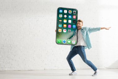 KYIV, UKRAINE - 21 Şubat 2020: Mutlu adam evde iPhone ekranlı akıllı telefon modelini tutarken başka tarafa bakıyor 