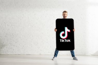 KYIV, UKRAINE - 21 Şubat 2020: Yakışıklı adam TikTok uygulaması ile akıllı telefonun büyük bir modelini tutuyor ve kameraya gülümsüyor 