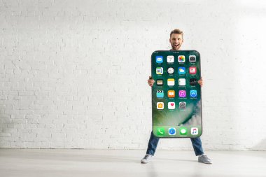 KYIV, UKRAINE - 21 Şubat 2020: Beyaz tuğla duvarın yanında iPhone ekranlı akıllı telefon modeli tutan neşeli adam