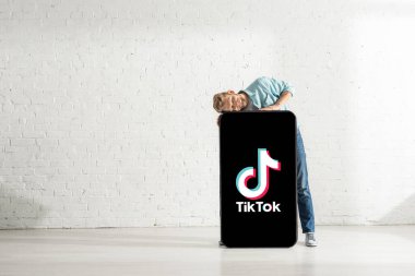 KYIV, UKRAINE - 21 Şubat 2020: Kapalı gözlü olumlu adam TikTok uygulaması ile dev akıllı telefon modelini kucaklıyor