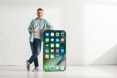 KYIV, UKRAINE - 21 Şubat 2020: Kameraya gülümseyen ve iPhone ekranlı akıllı telefonun büyük modelini gösteren yakışıklı adam 