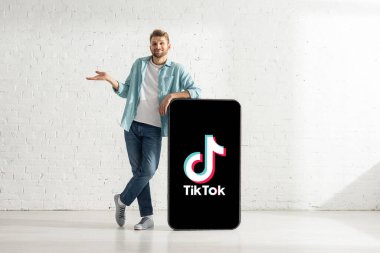 KYIV, UKRAINE - 21 Şubat 2020: Gülen adam TikTok uygulamalı akıllı telefonun büyük bir modelinin yanında şaşkın jest gösteriyor 