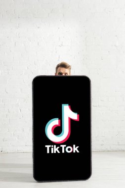 KYIV, UKRAINE - 21 Şubat 2020: TikTok uygulamalı büyük akıllı telefon modelinin yakınındaki kameraya bakan adam 