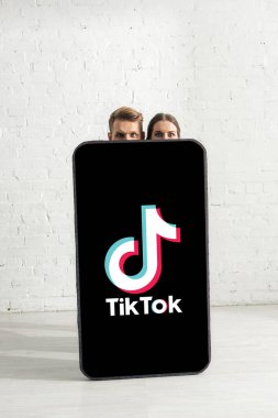 KYIV, UKRAINE - 21 Şubat 2020: Genç çift TikTok uygulamalı büyük akıllı telefon modelinin yanında kameraya bakıyor 