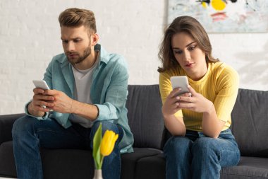 Evde kanepede otururken akıllı telefon kullanan genç çiftlerin seçici odağı 