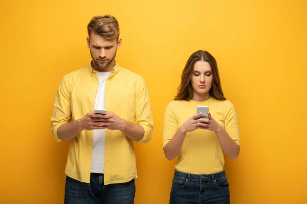 在黄色背景下使用智能手机的年轻夫妇 — 图库照片