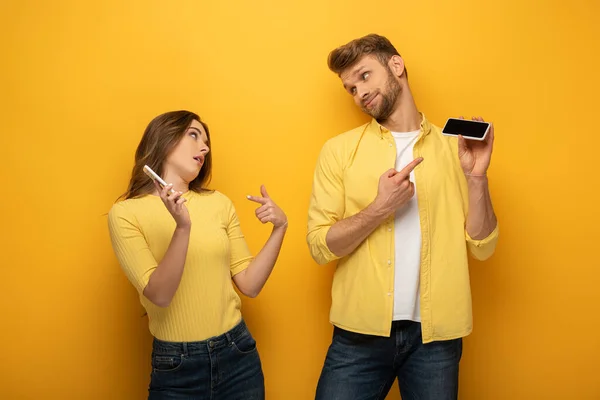 Couple Pointing Fingers Smartphones Looking Each Other Yellow Background — Stock Photo, Image