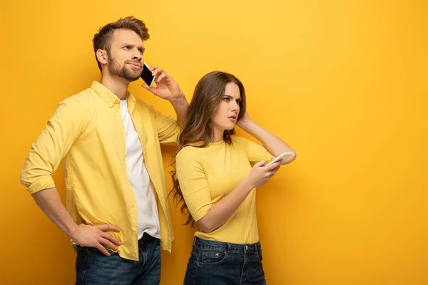 Casal Jovem Com Smartphones Olhando Para Fundo Amarelo — Fotografia de Stock