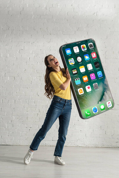 КИЕВ, Украина - 21 февраля 2020 года: Положительная женщина держит большую модель смартфона с экраном iphone дома
 