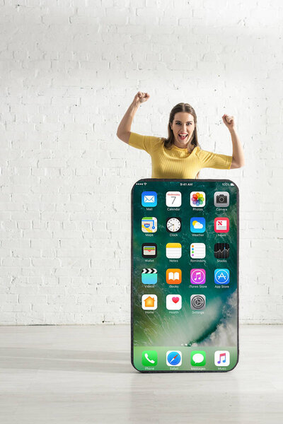 КИЕВ, УКРАИНА - 21 февраля 2020 года: Счастливая женщина показывает да жест рядом с огромной моделью смартфона с экраном iphone
 