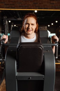 kasıtlı aşırı kilolu bir kız spor makinesinde kol uzatma egzersizi yapıyor.
