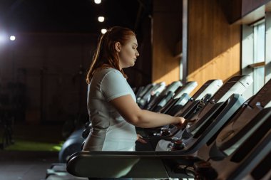 Spor salonundaki koşu bandındaki aşırı kilolu kız eğitiminin yan görünüşü