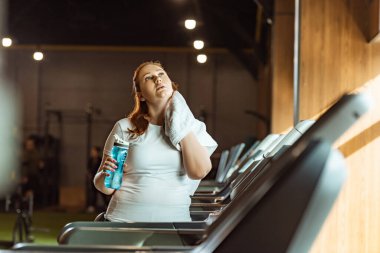 Spor şişesini tutarken boynu havluyla silen aşırı kilolu kız. 