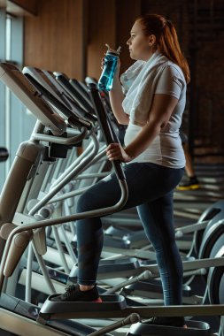 Atletizm antrenmanında spor şişesi tutan şişman kızın yan görünüşü