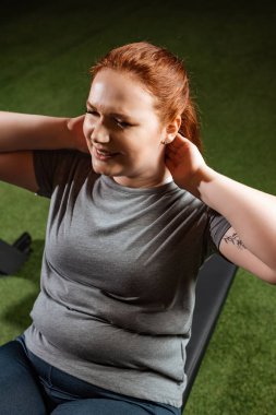 Maksatlı kilolu kızın fitness makinesi üzerinde karın kası egzersizi yaparken yüksek açılı görüntüsü 