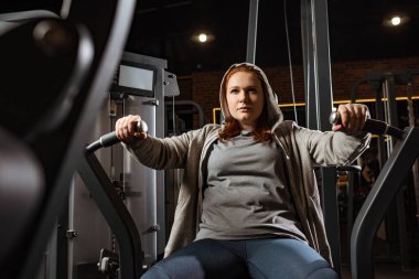 Kendine güvenen aşırı kilolu kızın fitness makinesi üzerinde kol uzatma egzersizi yapması. 