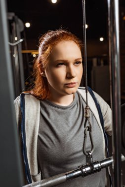 Kendine güvenen aşırı kilolu bir kızın eğitim makinesinde silah geliştirme egzersizi yapması.
