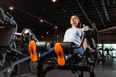 kasıtlı kilolu kız fitness makinesinde bacak uzatma egzersizi yapıyor.