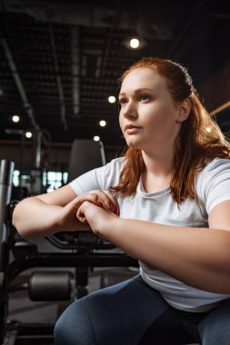 Kendine güveni tam, kilolu bir kız spor salonunda elleri sımsıkı bağlı oturuyor.