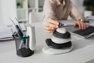 cropped view of businesswoman working with laptop at workplace with zen stones clipart