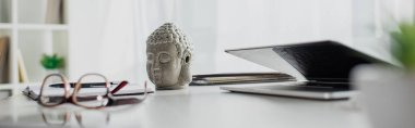 Buda 'nın kafasının panoramik görüntüsü, gözlük ve dizüstü bilgisayar modern ofisteki masada.