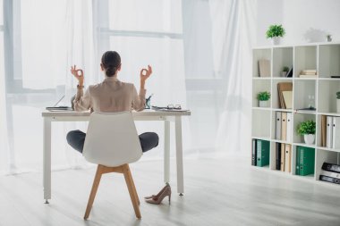 Back view of businesswoman meditating in lotus pose with gyan mudra at workplace  clipart