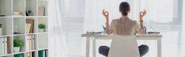 Nilüfer çiçeğiyle meditasyon yapan iş kadınının iş yerinde Gyan Mudra ile tütsü çubuğuyla poz verirken çekilmiş panoramik bir fotoğrafı.