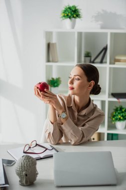 Güzel iş kadını iş yerinde Buda kafası ve dizüstü bilgisayarla elma tutuyor. 