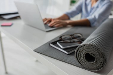 İş yerinde dizüstü bilgisayarda spor minderi, not defteri, akıllı telefon ve gözlükle çalışan iş kadını seçici odağı