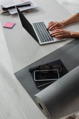 İş yerinde bilgisayarında spor paspası, not defteri, akıllı telefon ve gözlüklü bir iş kadını görüntüsü.