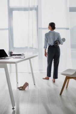 Ofiste yoga minderi tutan genç iş kadınının arka görüntüsü