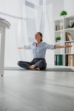 Genç iş kadını, ofiste Lotus pozisyonunda yoga yapıyor. 