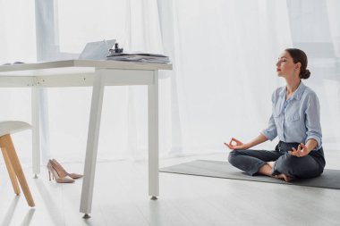 Genç iş kadını Lotus pozisyonunda yoga yapıyor. Ofiste Gyan Mudra ile birlikte. 