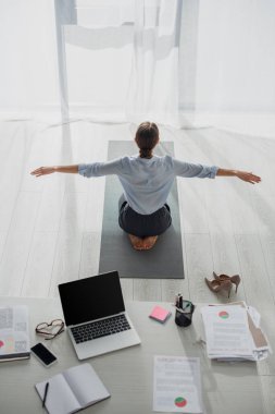 Nilüfer pozisyonunda dizüstü bilgisayarla yoga yapan iş kadınının arka görüntüsü