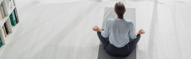 Nilüfer pozisyonunda yoga yapan iş kadınının panoramik görüntüsü ve ofisinde Gyan Mudra var. 