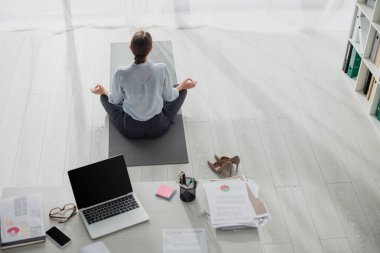 Nilüfer pozisyonunda yoga yapan iş kadınının arkadan görünüşü ve dizüstü bilgisayarlı Gyan Mudra.