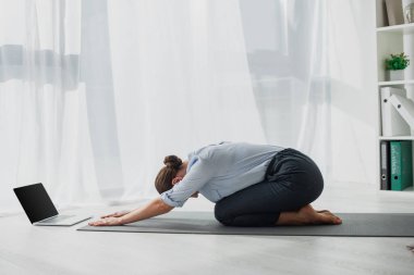 Çocuk Pozu 'ndaki genç iş kadını bilgisayarında yoga dersleri alıyor. 