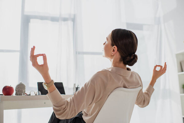 businesswoman meditating with closed eyes and gyan mudra at workplace in office 