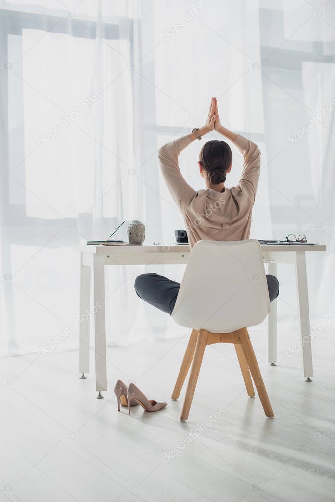 Back view of businesswoman meditating with namaste gesture at workplace with incense stick